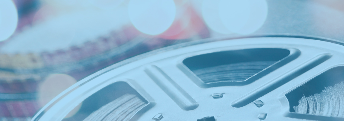 Close-up of a metal film reel with soft blurred colorful lights behind it, blue-toned and quiet
